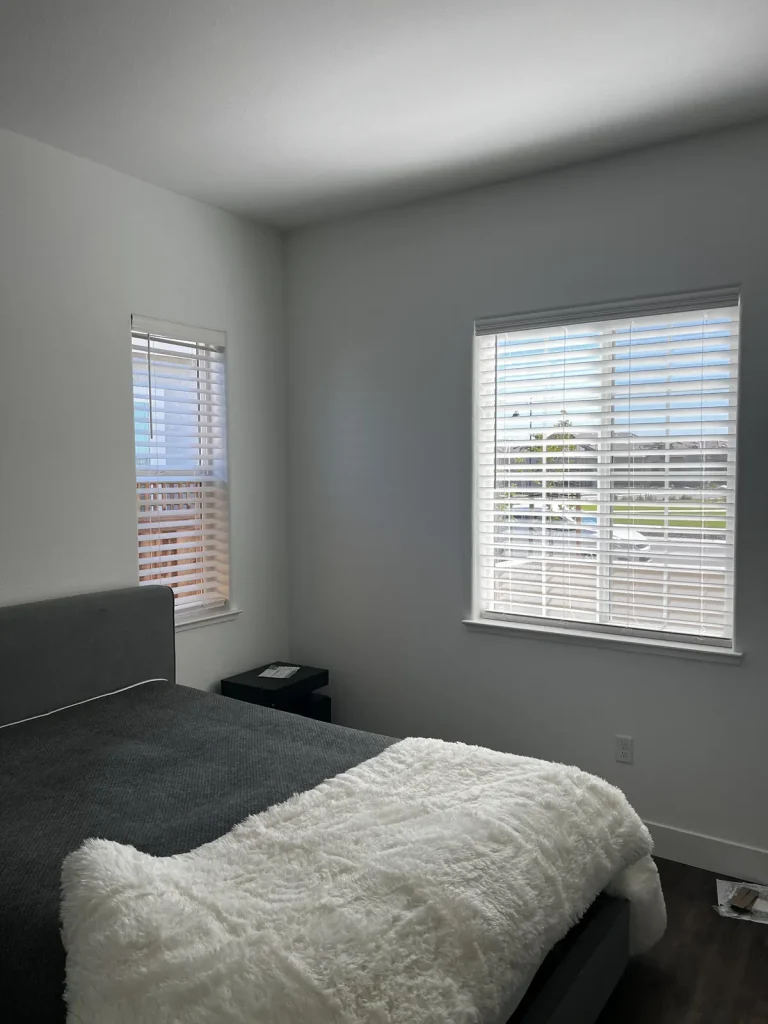 Faux wood blinds hung at two bedroom windows of different widths in Lathrop, each one cut to its own opening