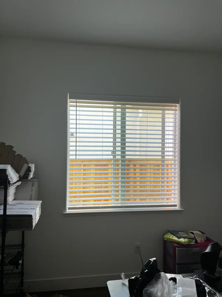 White faux wood blinds across a wide home office window in Lathrop, slats tilted part open over the fence line