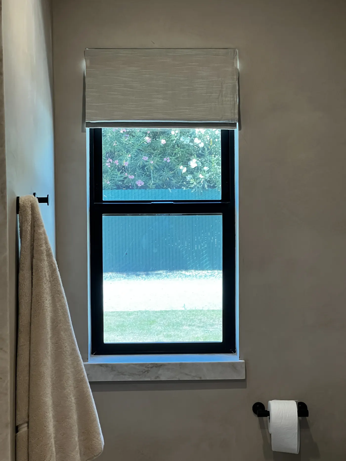 Woven wood shade mounted inside a bathroom window frame in Lodi, drawn back to the top of the opening against a plaster wall