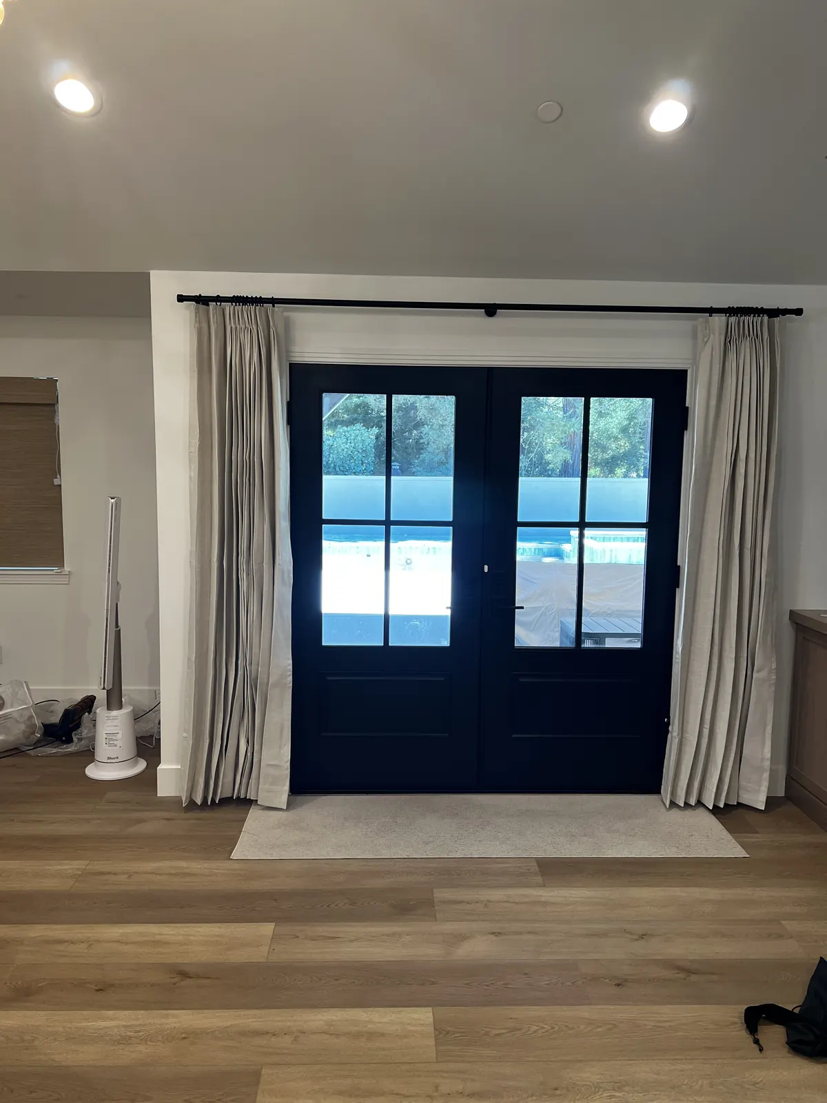 Linen drapery panels hung on a black rod across the glazed entry door of a Lodi home, stacked back either side of the glass