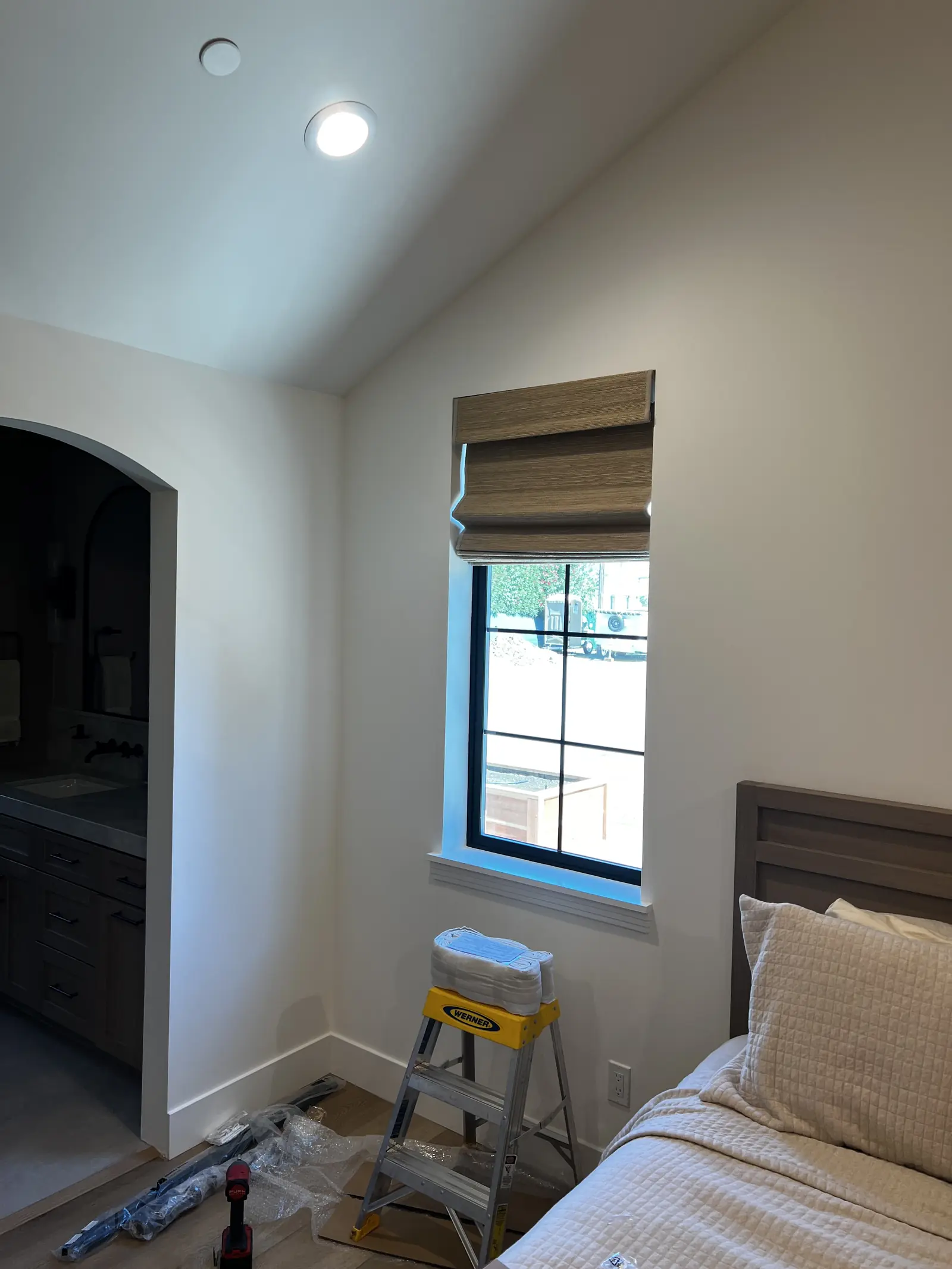 Woven wood roman shade hung at a vaulted bedroom window in Lodi, folds stacked above the glass with the step ladder still standing