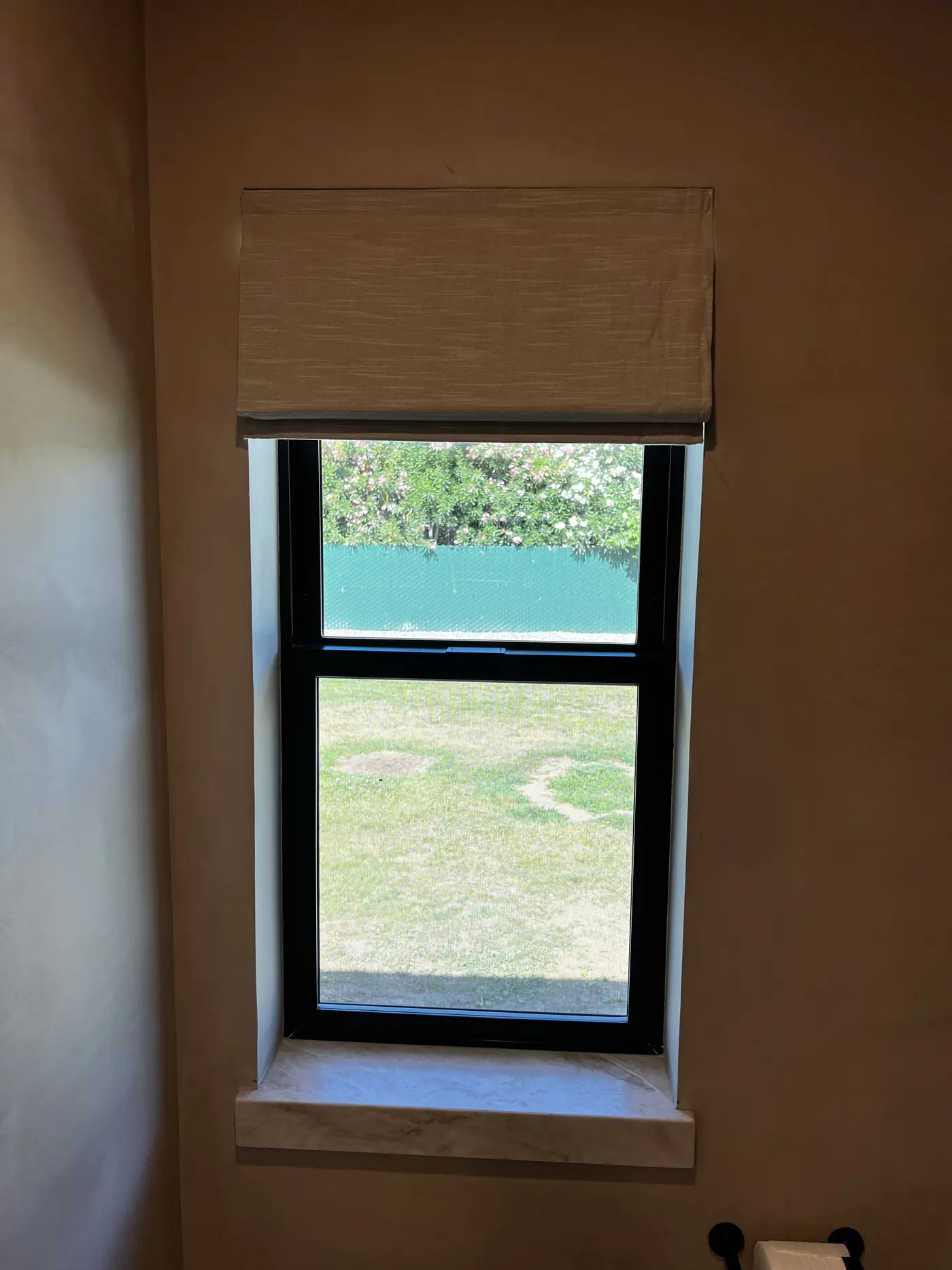 Woven wood roman shade fitted to a narrow bathroom window in Lodi, mounted above the marble sill against a clay plaster wall