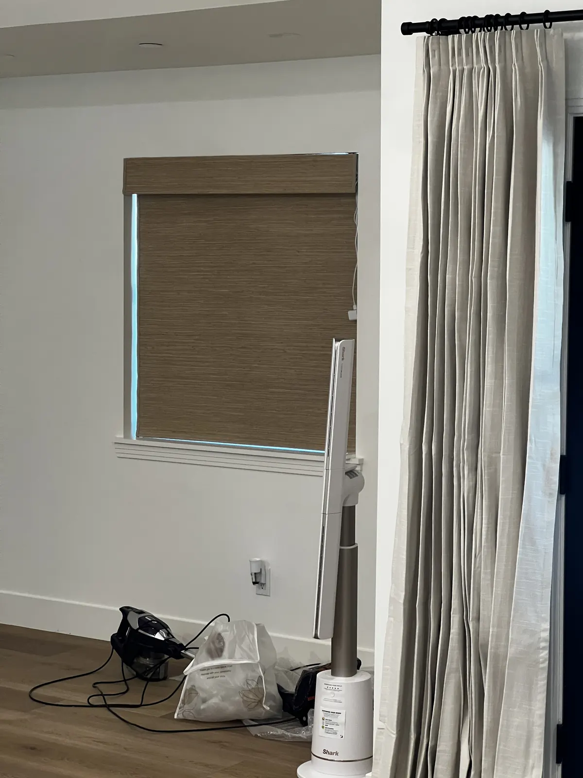 A woven wood roller shade and a pleated linen drapery panel in the same Lodi room, the shade inside the frame and the panel on a black rod