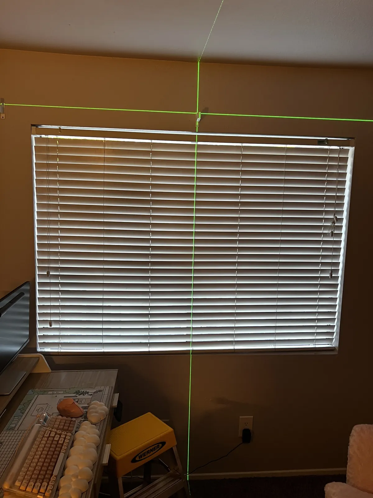 White horizontal blinds across a wide home office window in Sacramento, with the cross line laser still lit above the headrail